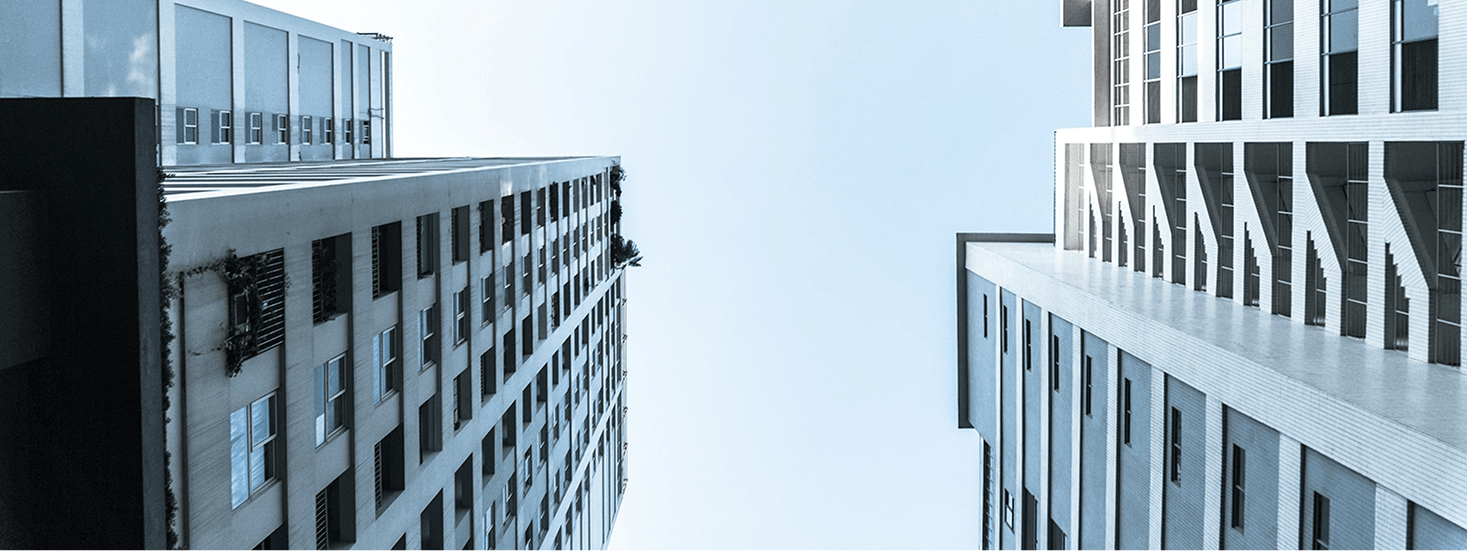 A low-angle view of two modern high-rise buildings with large windows and geometric architectural details, set against a clear blue sky.